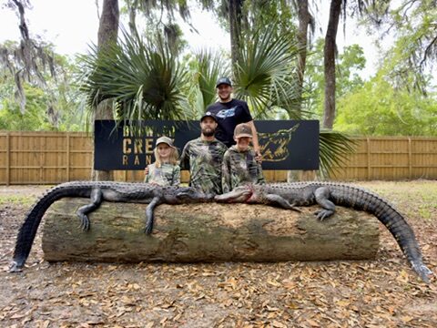 A family with two trophy alligators under the Brawler Creek Ranch sign