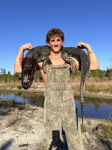 A young hunter holding a harvested alligator across his shoulders